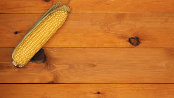 Hands put corn and knife on the table. A man lays out corn on the cob with green leaves and husks 