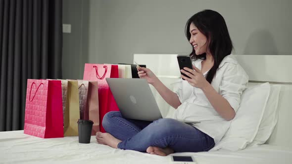 happy woman using smartphone for online shopping with credit card on a bed