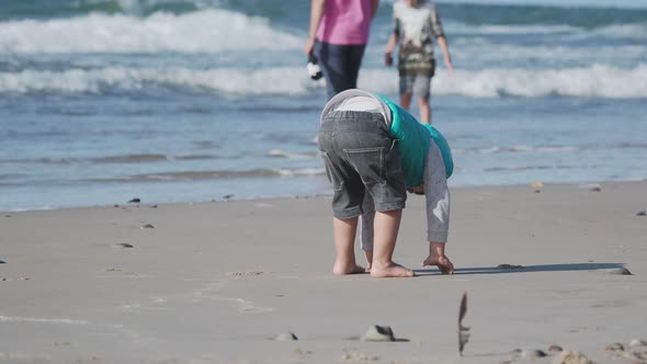 Toddler Boy in Waistcoat Is Playing with Sand on Sea Side. alt