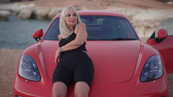 Mature Caucasian Confident Woman Leaning on Car Hoods Looking Around Outdoors alt