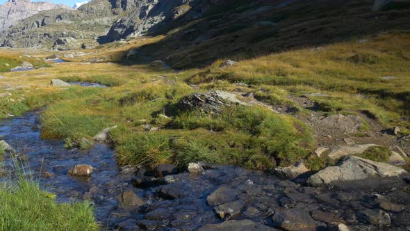 Alpine landscape, high mountain stream in uncontaminated environment amid rocks and meadows alt