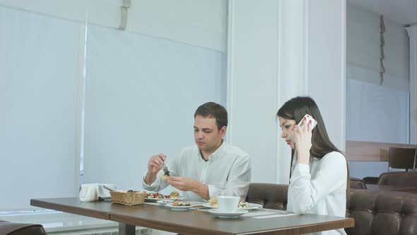 Young Man Eating While His Girlfriend Talking on the Phone at Restaurant alt