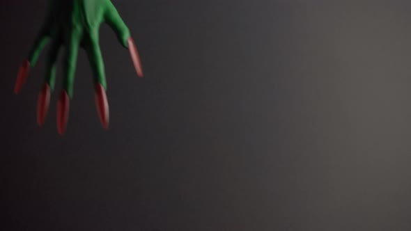 Green Witches Hands Appears From Behind a Black Background with Copyspace