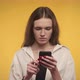Young Adult Caucasian Woman Recieving Great News on Her Smart Phone on a Bright Yellow Background