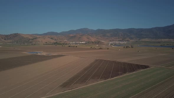 Aerial view of empty farmland crop fields surrounded by California mountains alt