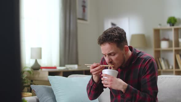 Young Handsome Man Lunchs Chinese Noodle From Delivery and Watching Tv at Home in the Living Room alt