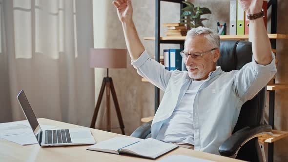 Mature Businessman Putting Hands Behind His Head and Smiling Being Happy Sitting at Table with alt