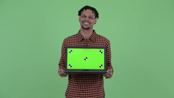 Happy Young Handsome African Man Thinking While Showing Laptop alt