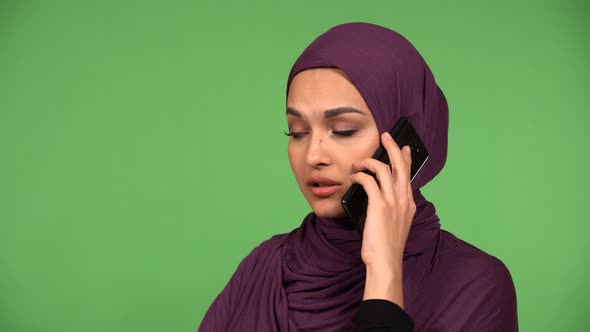 A Young Beautiful Muslim Woman Talks on a Smartphone with a Smile  Closeup Green Screen Background