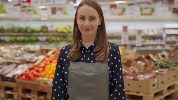 Portrait of a Female Worker in an Apron Against a Background of Fruits a Young Woman Crosses Her alt
