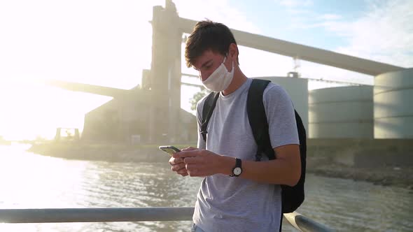Man With Face Mask And Backpack Using Smartphone Near Port In Ingeniero White, Buenos Aires, Argenti alt