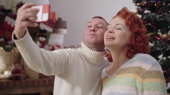 Happy Adult Couple Taking Selfie with Decorated Christmas Tree at Background alt