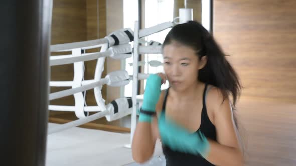 Asian Woman Kick Boxer Punching Bag in Gym