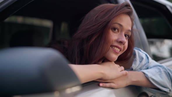 Closeup Portrait of Smiling Happy Young Beautiful Lady Sitting in Car Admiring Nature in Forest alt