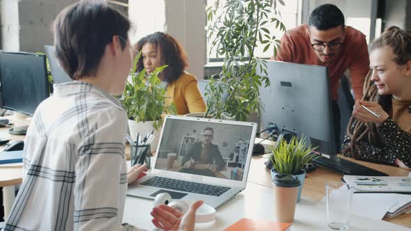Young Woman Talking To Male Colleague Through Video Call Using Laptop in Open Plan Office alt