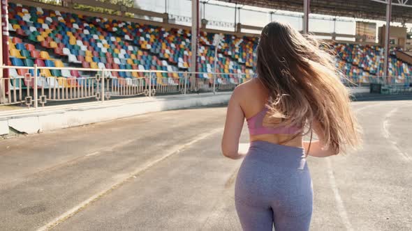 Back View of Beautiful Young Woman Jogging at Sports Stadium alt