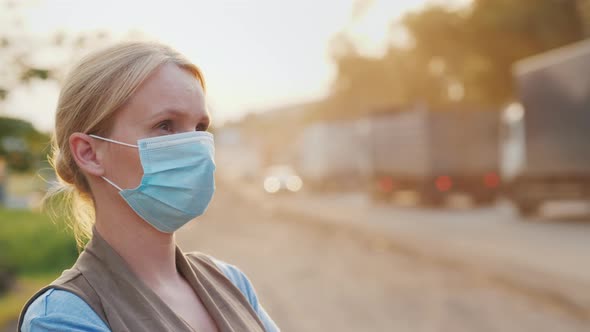 A Woman in a Protective Mask on a Dusty Road alt