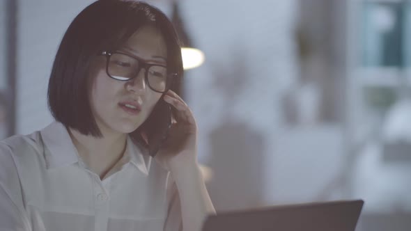 Asian Woman Talking on Phone in Office in Evening alt