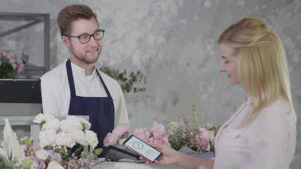 Contactless Payment, Male Seller in Flower Shop Sells Bouquet of Flowers To Female Buyer Pays alt