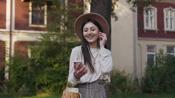 Woman in Beige Hat Listening Nice Music on Headphones During Her Walk alt