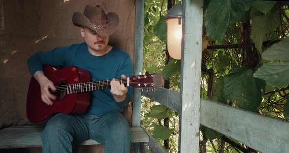 Man with an Acoustic Guitar is Sitting on Porch of House Playing an Instrument alt