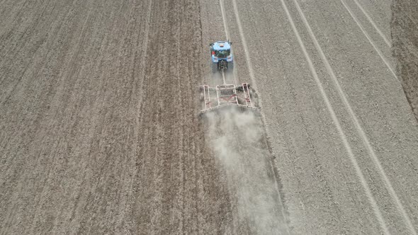 Soil being prepared with discs with perfectly straight rows. Clouds of dust. Tree lined fields.