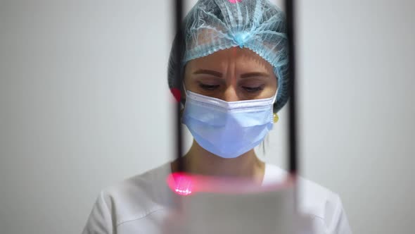 Concentrated Caucasian Woman in Face Mask Thinking Analyzing Xray Image of Teeth and Jaw Standing at alt