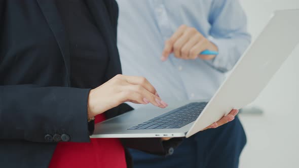 Woman Holding a Laptop and Pressing Laptop Keys in the Office with Another Employee. alt