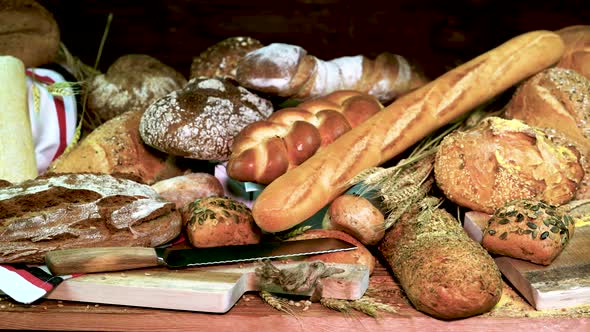 Assortment of Fresh Bread with Wheat and a Knife for Cutting Bread on a Dark Wooden Background alt