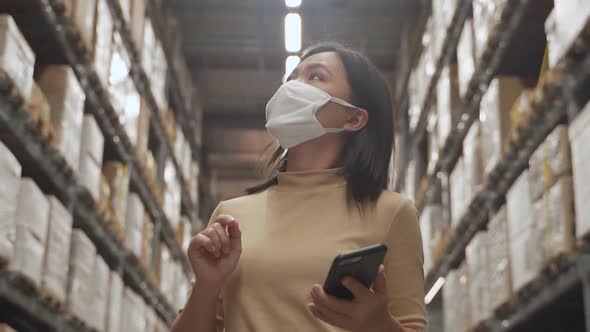 Asian woman wearing mask walking in warehouse and use smart phone.