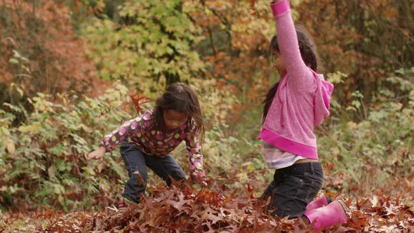 Two young girls in Fall throwing pile of leaves