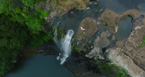 A Beautiful Woman in a White Dress on Top of a Waterfall in a Green Jungle Enjoys Her Victory alt