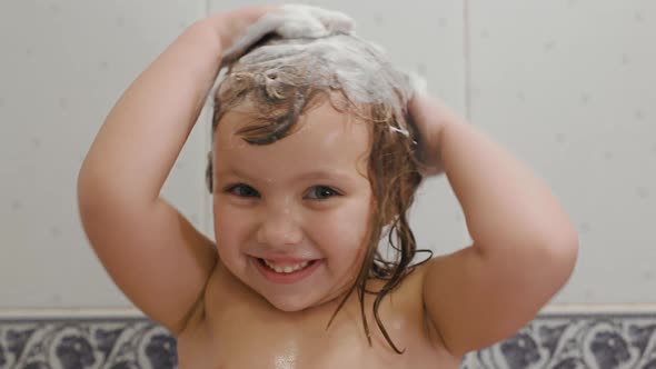Cute Little Girl Shampoos Her Hair Looks at Foam at Hands and Smiles