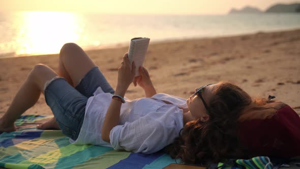 A Young Woman Reading a Book and Relaxing on the Beach alt