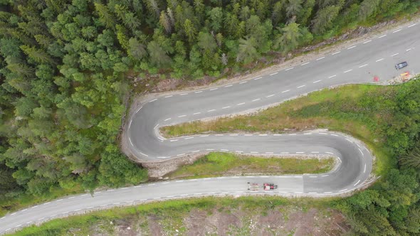 Tractor driving down winding mountain forest road hairpins, aerial top down view alt