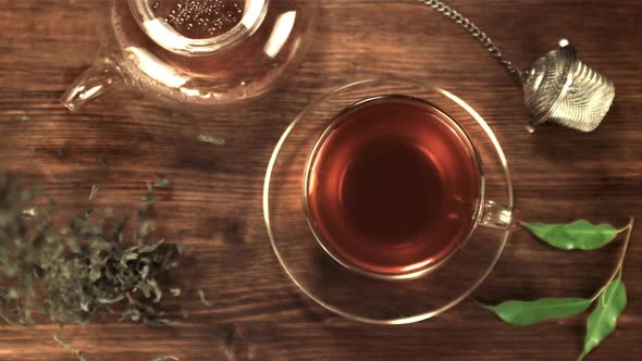 Super Slow Motion Dry Tea Leaves Fall on the Table Next to the Tea in the Cup alt