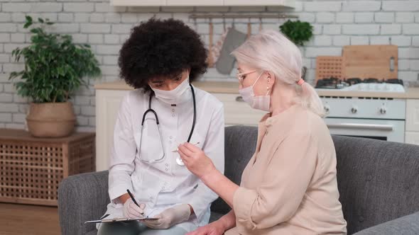 Afro American Woman Doctor in Mask Looks at Body Temperature Senor Woman Looking at Thermometer alt