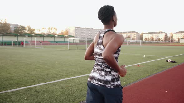 A Young Black Girl Training at the City Stadium and Runs on the Treadmill Around the Football Field alt