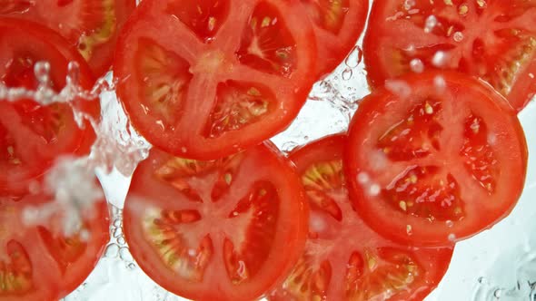 Super Slow Motion Shot of Tomato Slices Falling Into Water on White Background at 1000Fps. alt