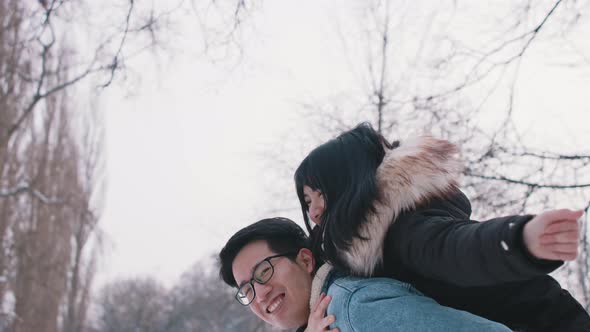 Young Man Giving Piggyback Ride To His Girlfriend and Spinning Her in the Park on Snowy Winter Day alt