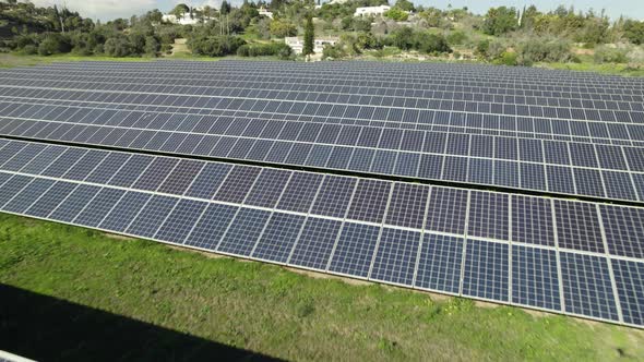 Long rows of solar panels on big solar farm; low drone pullback
