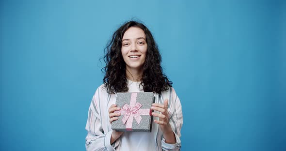 A Young Woman Opens a Gift in a Beautifully Packaged Box on a Blue Background alt