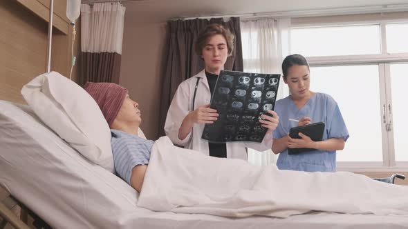 Female doctor explains x-ray film to patient at inpatient room bed in hospital. alt