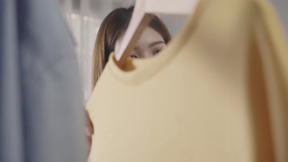 Beautiful young Asian woman choosing her fashion outfit clothes in closet at home or store. alt