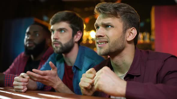 Caucasian and Black Male Friends Watching Football Game in Bar, Team Losing alt