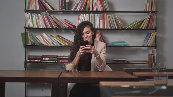 Girl Texting On Phone With Book Shelf In Background At Cafe Restaurant alt