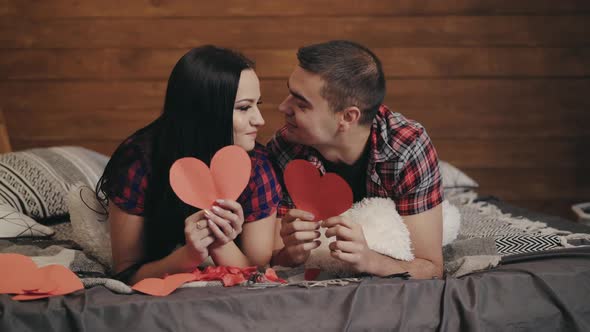 couple in love are kissing under the guise of handmade hearts in the bedroom alt