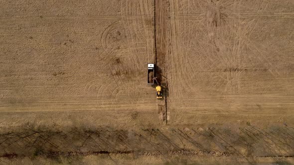 Yellow excavator digs the ground and loads it on a truck. Top view. alt