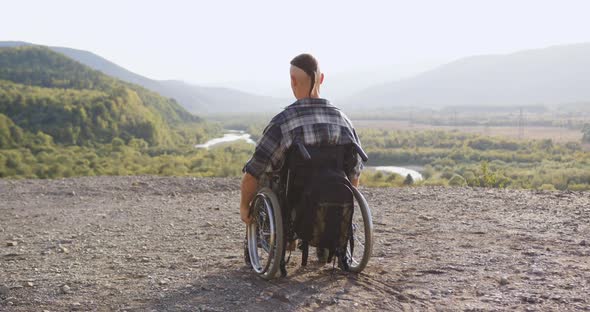 Man in Wheelchair Which Riding Up to the End of Hill to Look Around alt