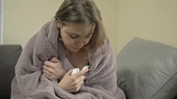 Young Woman Sits Wrapped in a Blanket and Measures the Temperature alt